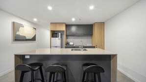 A modern kitchen with a central island, bar stools, and a microwave. - Chic Inner-City 2-Bed Abode with Pool, Gym & Sauna (Braddon)