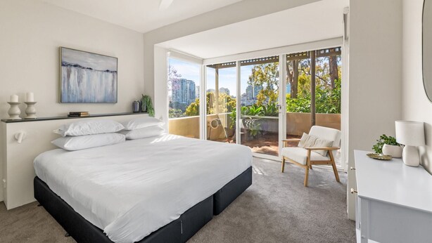 Un dormitorio moderno con una cama grande, un balcón con vistas a la ciudad y un ventilador de techo.
