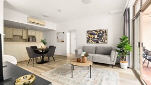 A modern living room with a grey sofa, a coffee table, and a dining area with a table and chairs. - Bright Inner-West Stay with Pool Access (Camperdown)