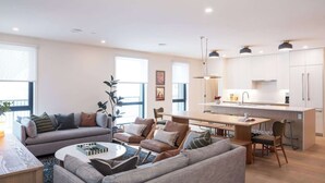 A modern living room with a sofa, coffee table, and a dining area with a bench. - Revelstoke - Revel And Rest-New condo! (Revelstoke)
