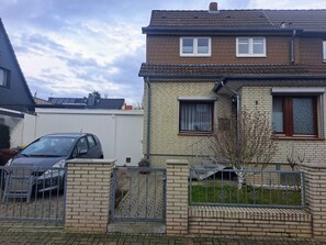 A residential building with a brick facade, two windows with curtains, and a car parked in the driveway. - Apartment 'Algetet' with Shared Terrace, Garden, and Wi-Fi (Hannover)