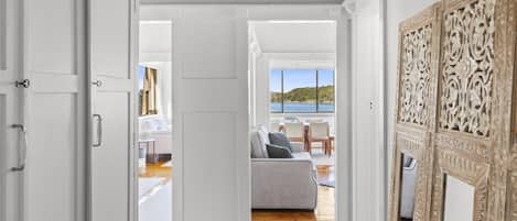An open doorway leading to a living area with a sofa, a dining table, and a view of the sea.