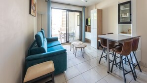 A compact living space with a sofa, a dining table with chairs, a small kitchen area, and a sliding glass door leading to an outdoor area. - Waterfront Riviera Charm with a View (Mandelieu-la-Napoule)