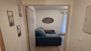 A hallway leading to a living room with a blue sofa, patterned cushions, and a wall-mounted decorative piece. - Alpine Nook in the Heart of Allos (Allos)