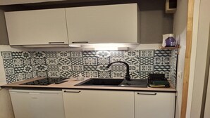 A compact kitchen with a black sink, white cabinets, and patterned backsplash tiles. - Alpine Nook in the Heart of Allos (Allos)