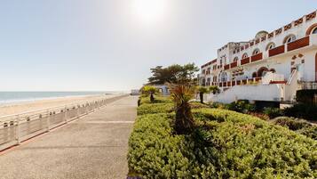 Un hotel frente al mar con un paseo marítimo, un camino bordeado de palmeras y vistas al océano.