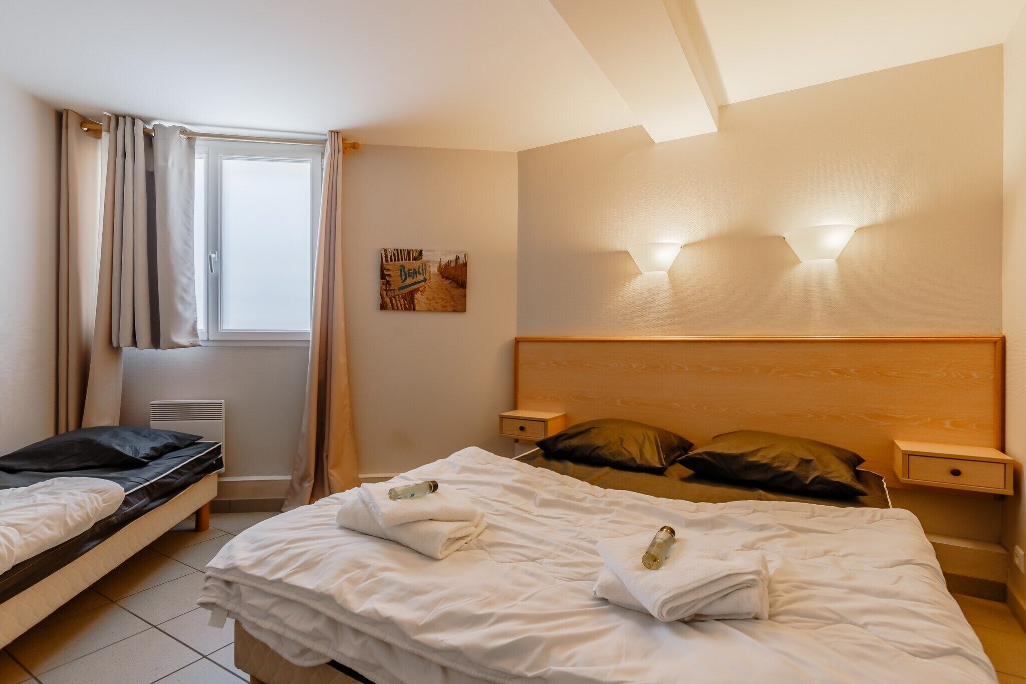 Una habitación de hotel con cama, mesita de noche, cortinas y una lámpara de pared.