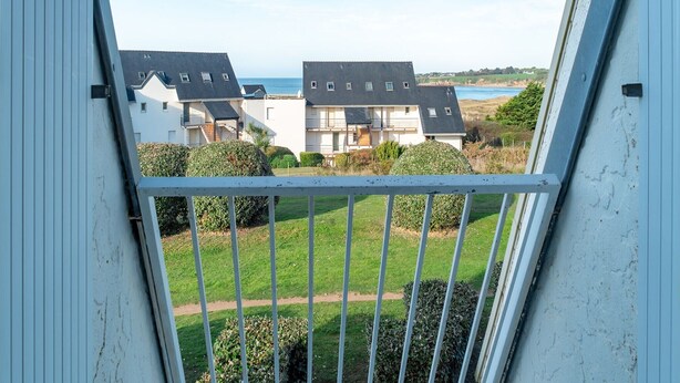 A view from a balcony with a metal railing, overlooking a residential area with houses and a body of water in the background.