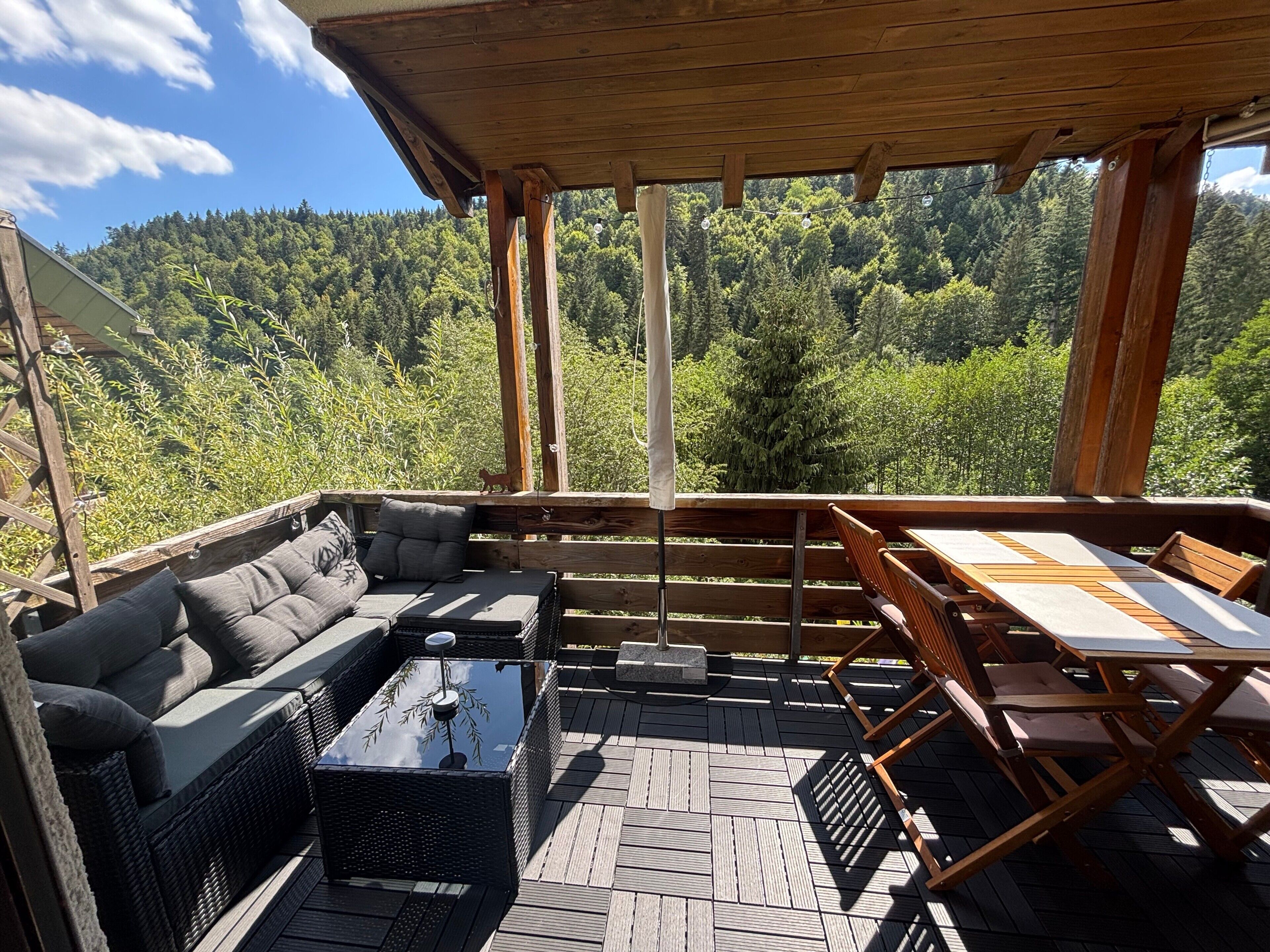 Ein überdachter Außenbereich mit einer Couch, einem Tisch und Stühlen mit Blick auf eine bewaldete Landschaft.
