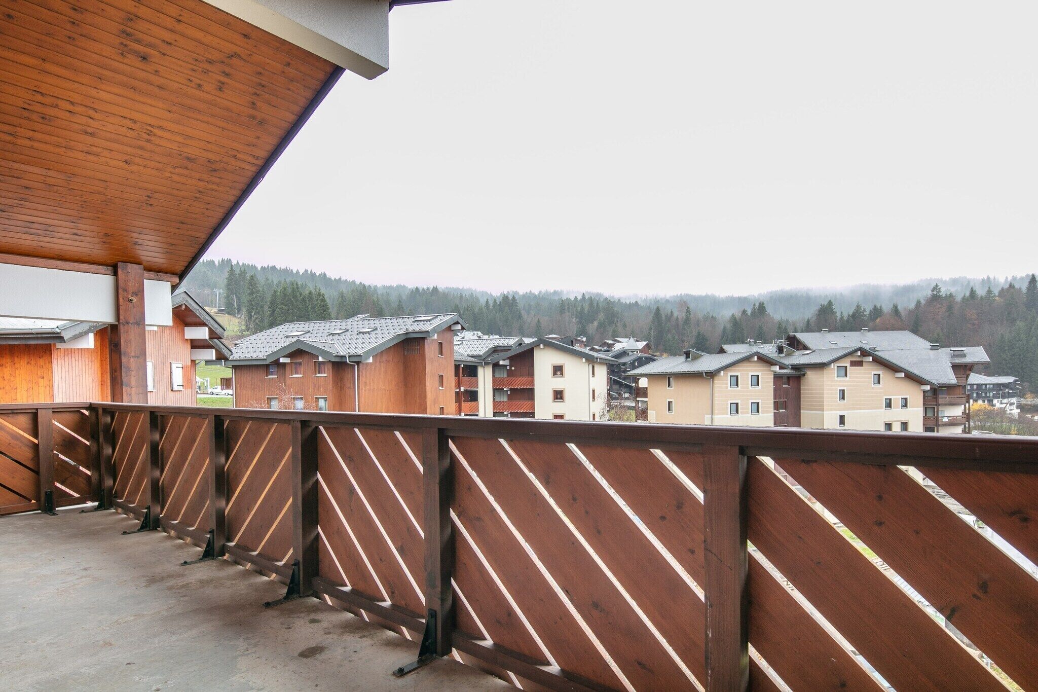 A wooden balcony with a view of residential buildings and a forested hillside.