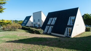 Fila de casas modernas con techos triangulares, paredes blancas y techos oscuros, ubicadas en un área verde con árboles al fondo.
