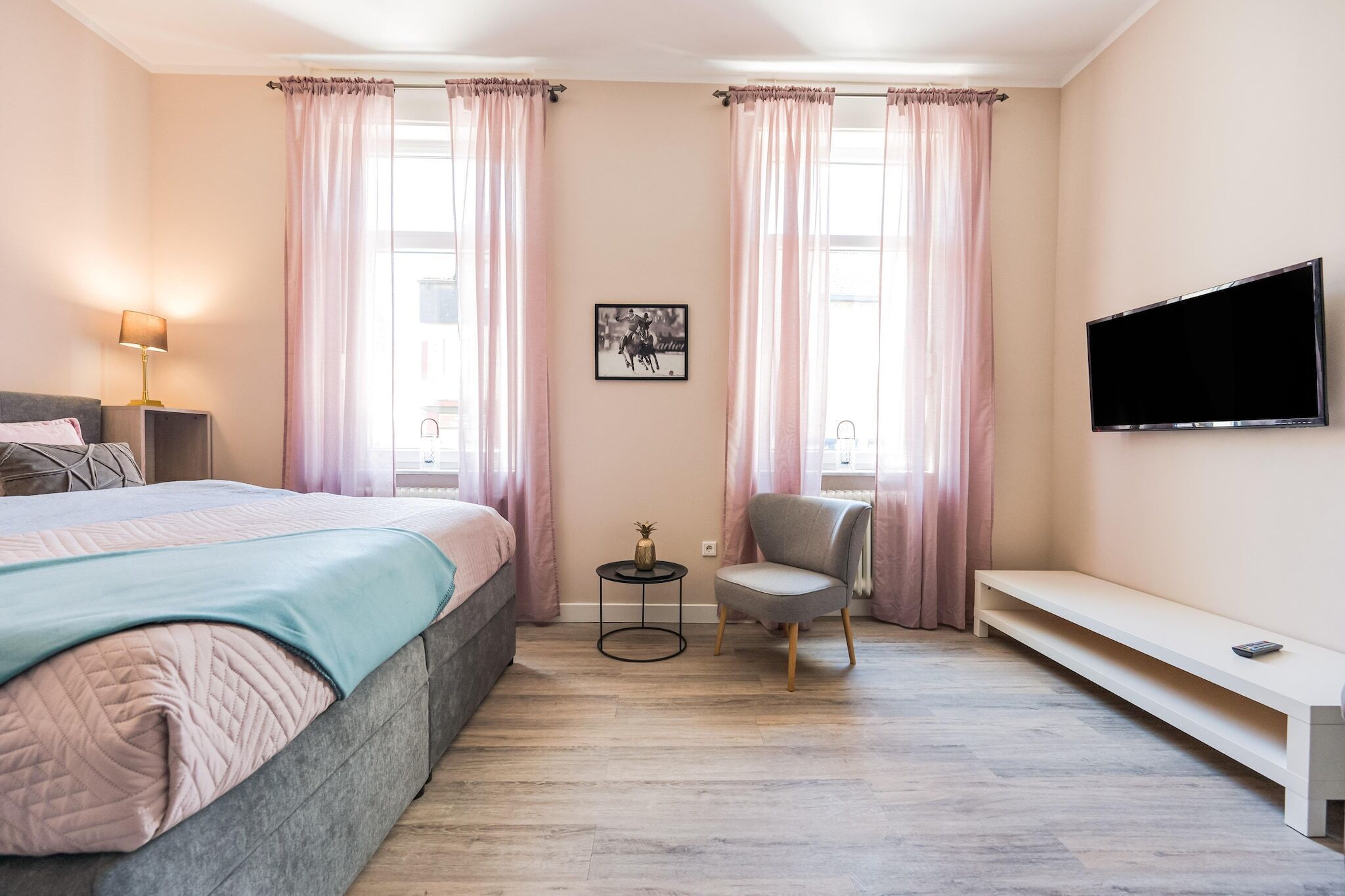 Ein Schlafzimmer mit einem Bett, einem Sessel, einem kleinen Tisch, einer Bank und einem an der Wand befestigten Fernseher.