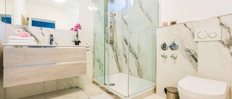 Un baño moderno con ducha de vidrio, piso de mármol y un inodoro blanco.