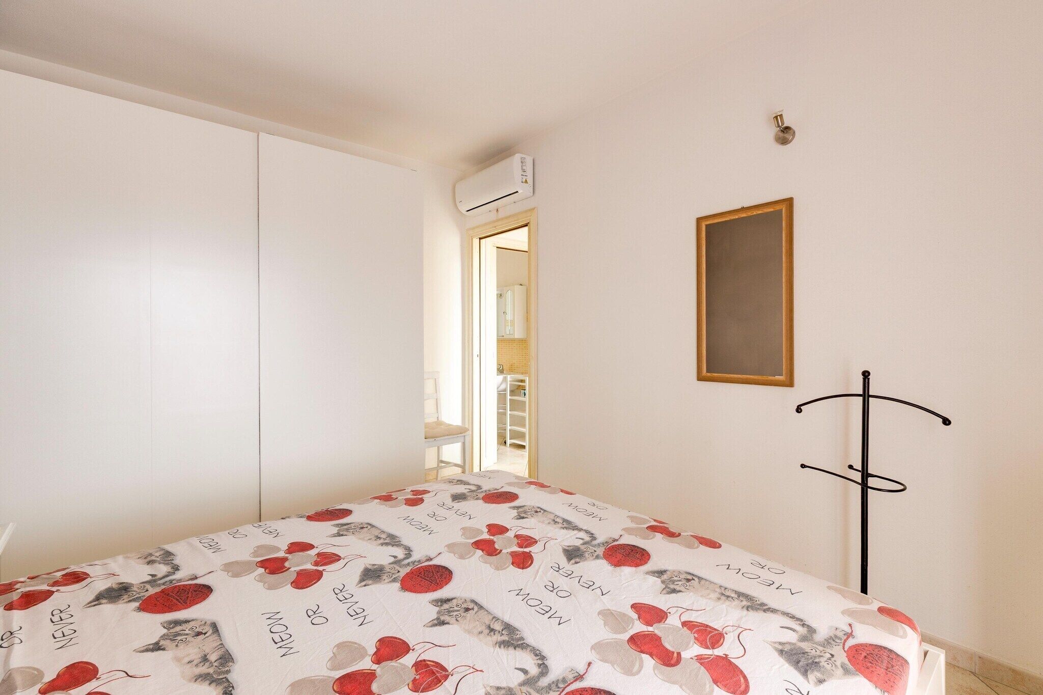 Ein Schlafzimmer mit Bett, Kleiderschrank, Klimaanlage, Kleiderständer und einer Tür zu einem anderen Raum.