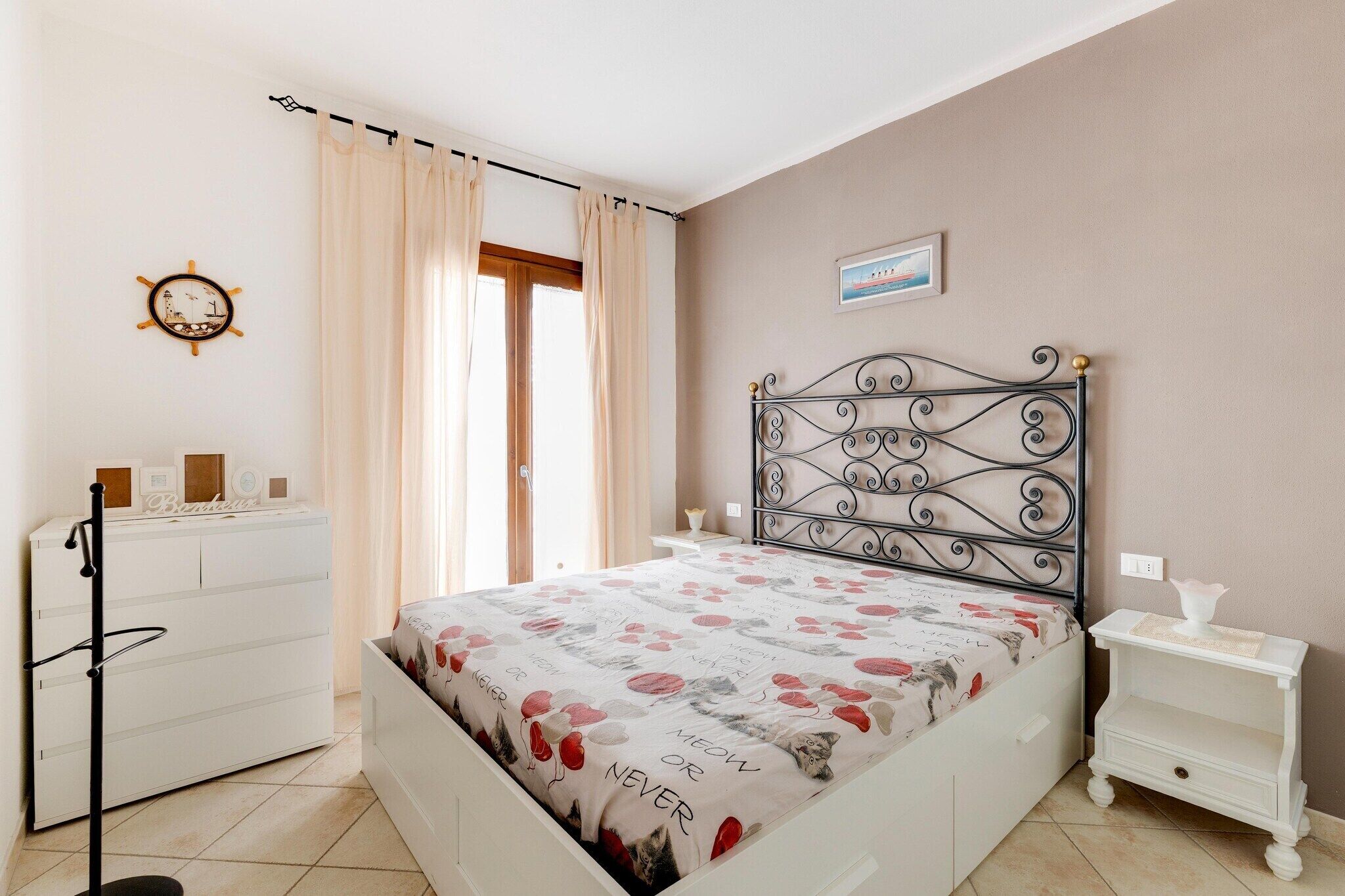 A bedroom with a bed, a dresser, a nightstand, a clock, and a window with curtains.