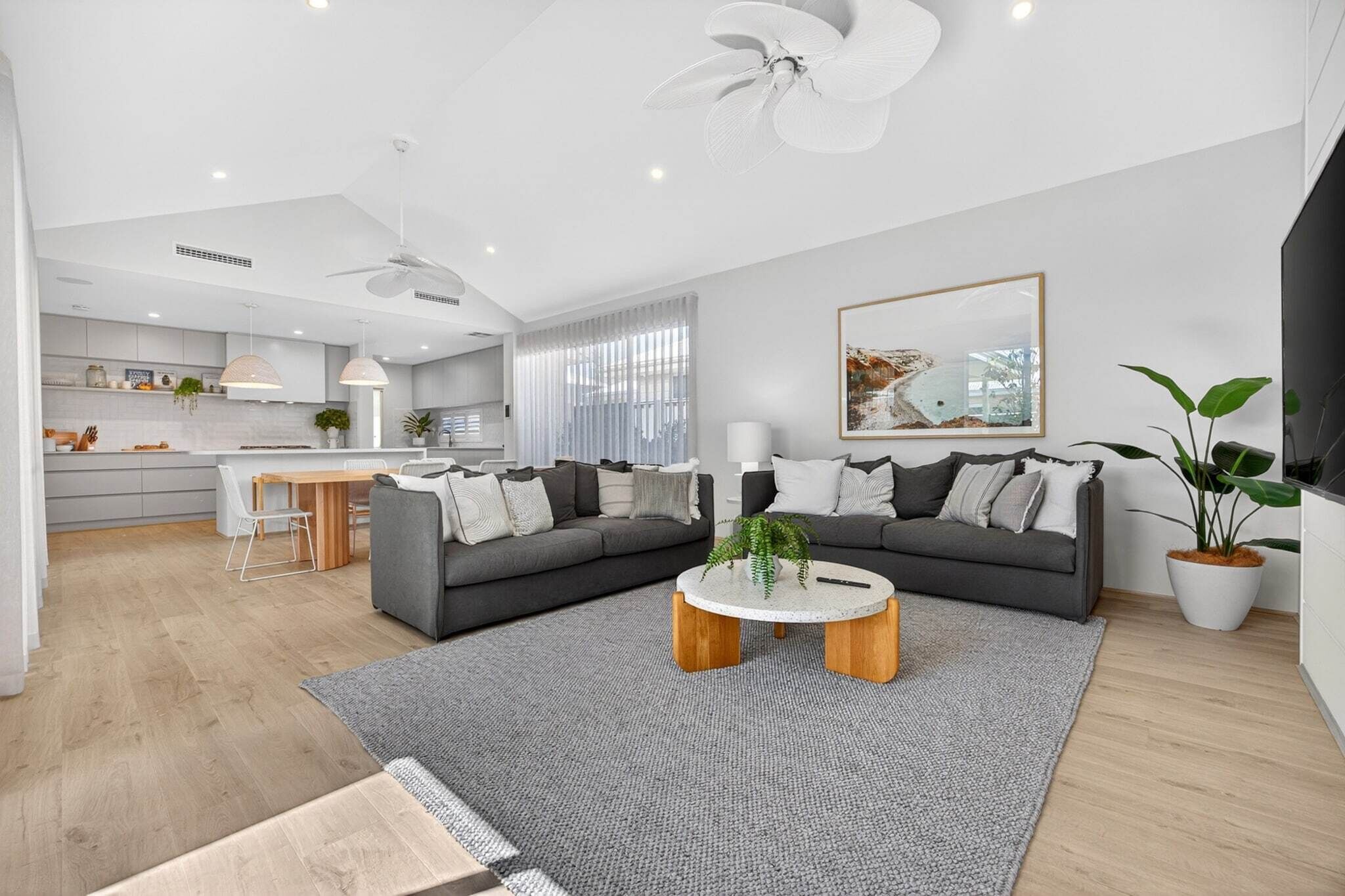 Una sala de estar moderna con un sofá gris, una mesa de centro y una zona de comedor con una cocina al fondo.
