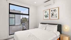 Ein modernes Hotelzimmer mit einem großen Fenster, einem Bett mit weißer Bettwäsche und zwei gerahmten Pflanzenbildern an der Wand.