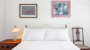 Cama bem arrumada com lençóis brancos, luminária de cabeceira e uma pintura abstrata emoldurada acima.