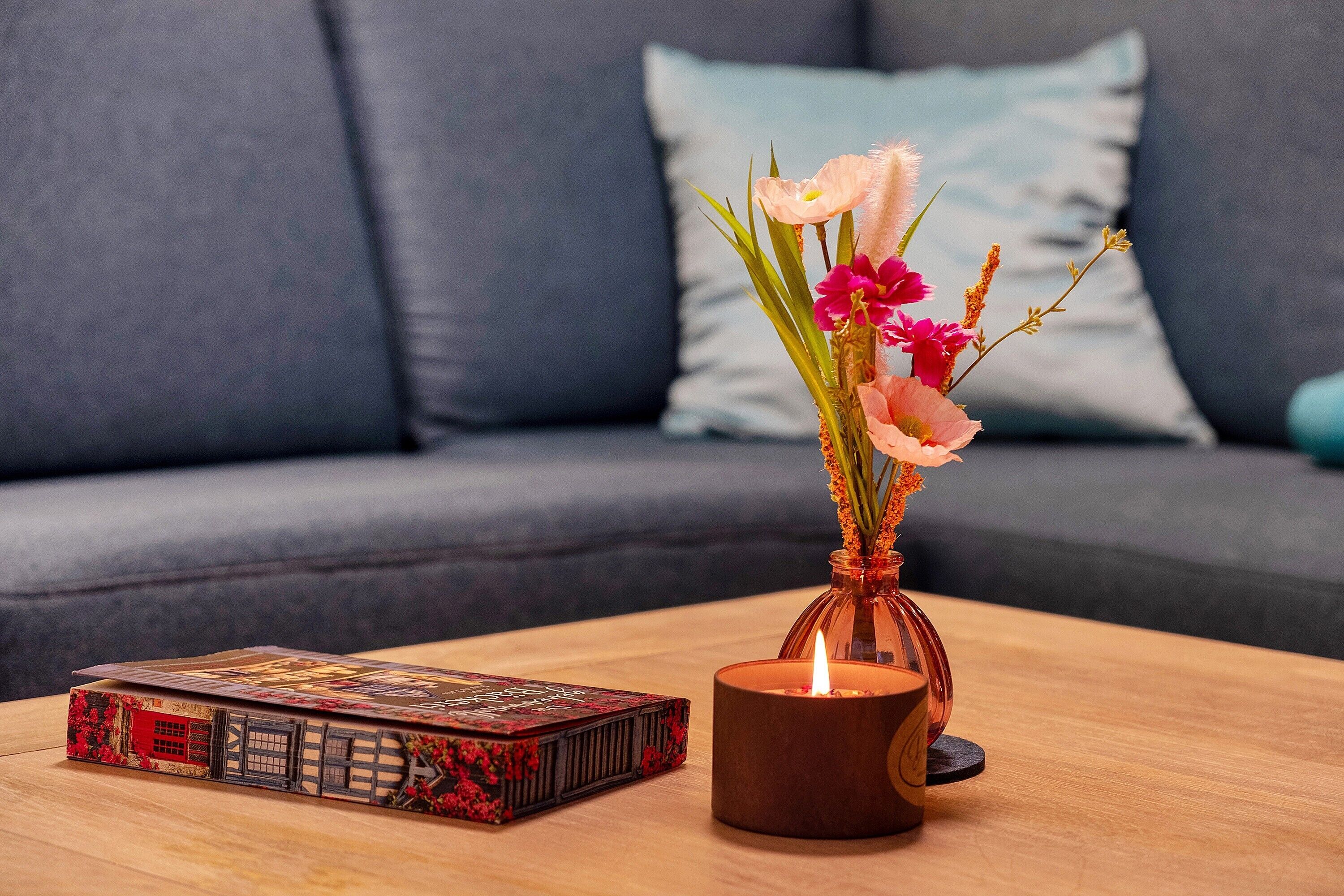 Um livro, uma vela e um vaso com flores sobre uma mesa de madeira.