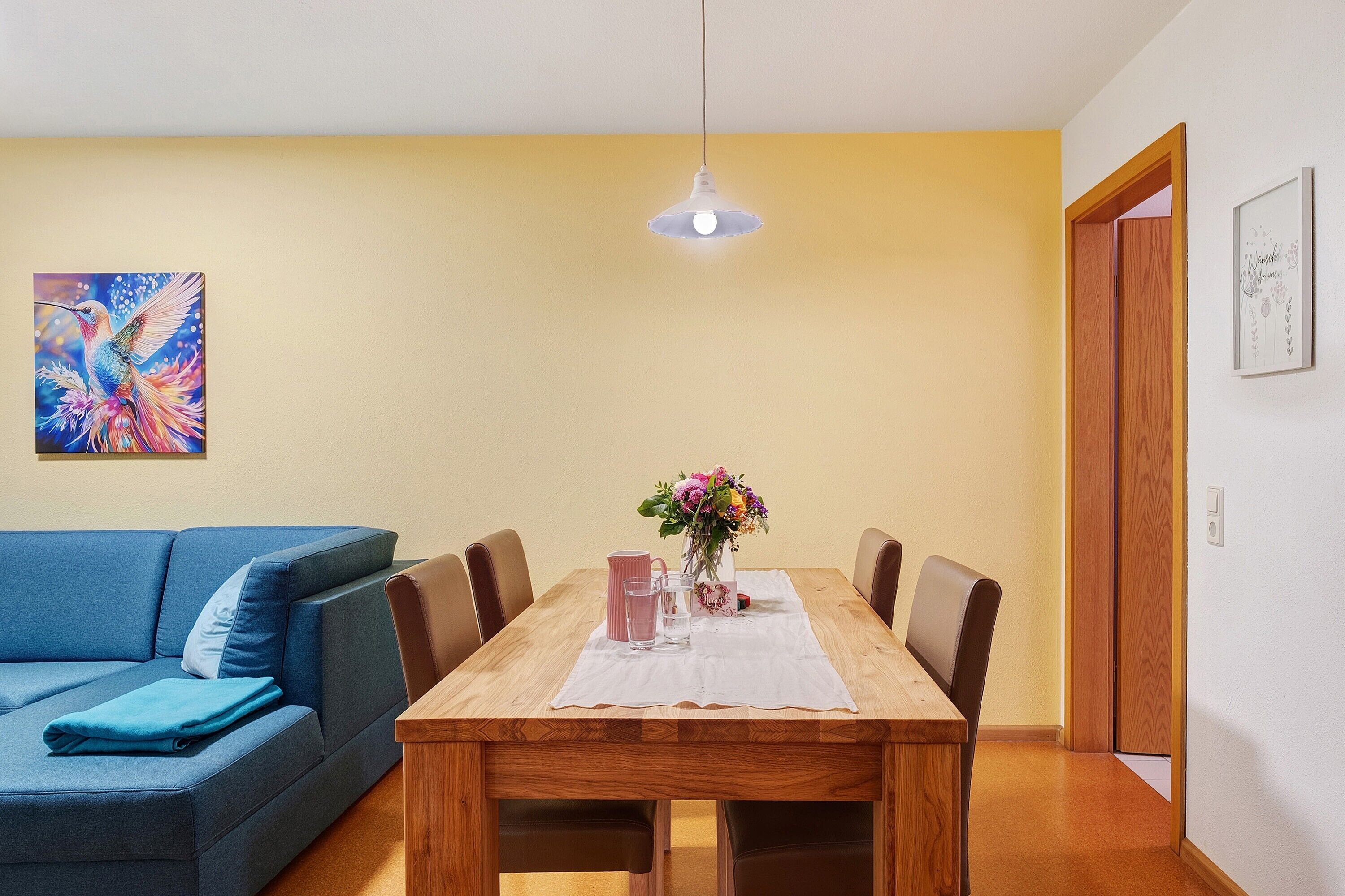 Ein Essbereich mit Holztisch, Stühlen, einem blauen Sofa, einer Hängeleuchte und einem Bild an der Wand.