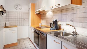 Una cocina moderna con armarios blancos, un lavamanos de acero inoxidable, una cafetera y un reloj en la pared.