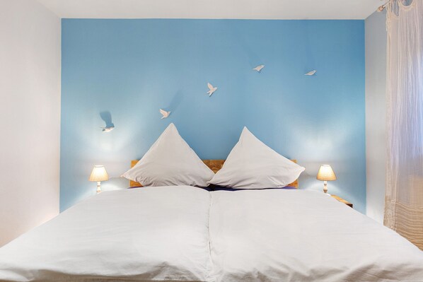 A bed with white bedding, two bedside lamps, and a blue wall with white bird silhouettes.