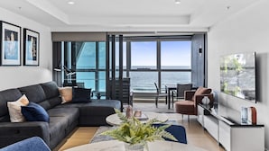 Un salon moderne doté d’une grande fenêtre donnant sur la mer, d’un canapé en cuir noir, d’une table basse et d’un téléviseur à écran plat.