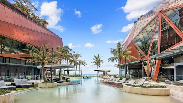 Un hôtel moderne doté d’une piscine, de palmiers et offrant une vue sur un ciel dégagé.