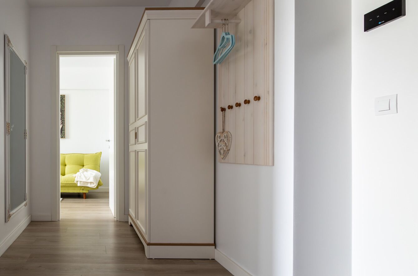 Un pasillo con piso de madera, una puerta blanca con un adorno con forma de corazón y un interruptor de luz en la pared.