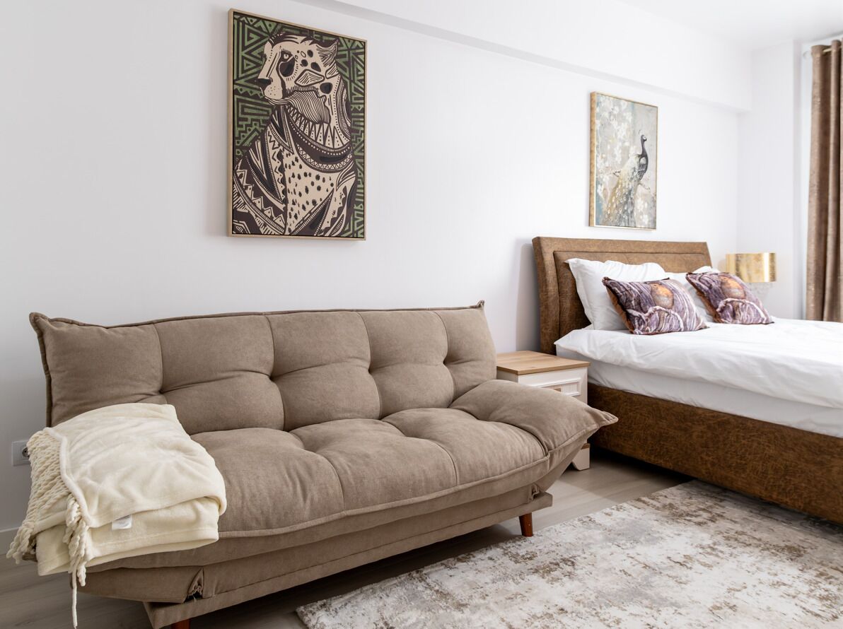 A modern bedroom with a sofa, a bed, and two wall-mounted artworks.