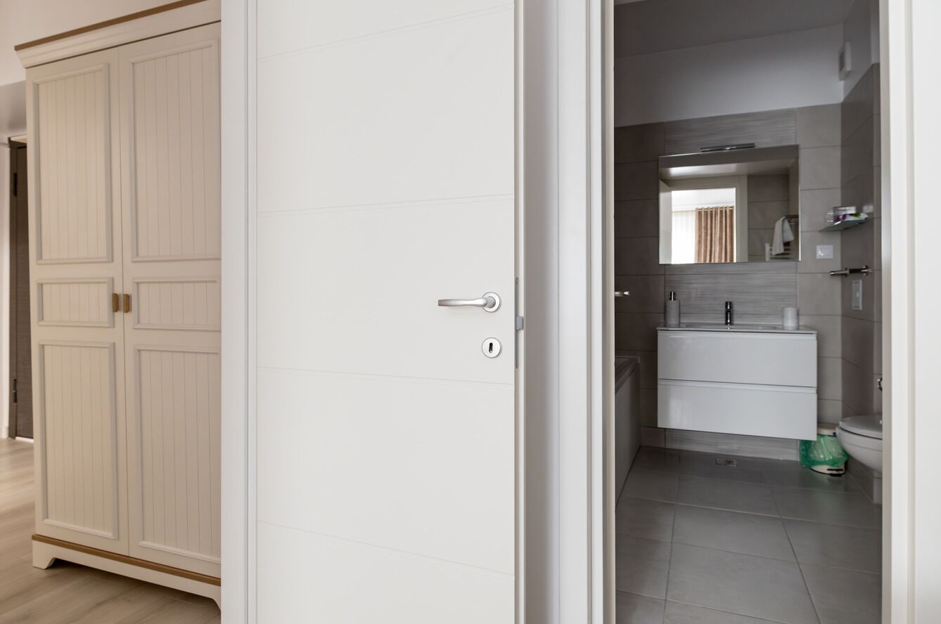 Ein Zimmer mit einem weißen Kleiderschrank, ein Badezimmer mit Waschbecken und Spiegel sowie ein grüner Mülleimer.