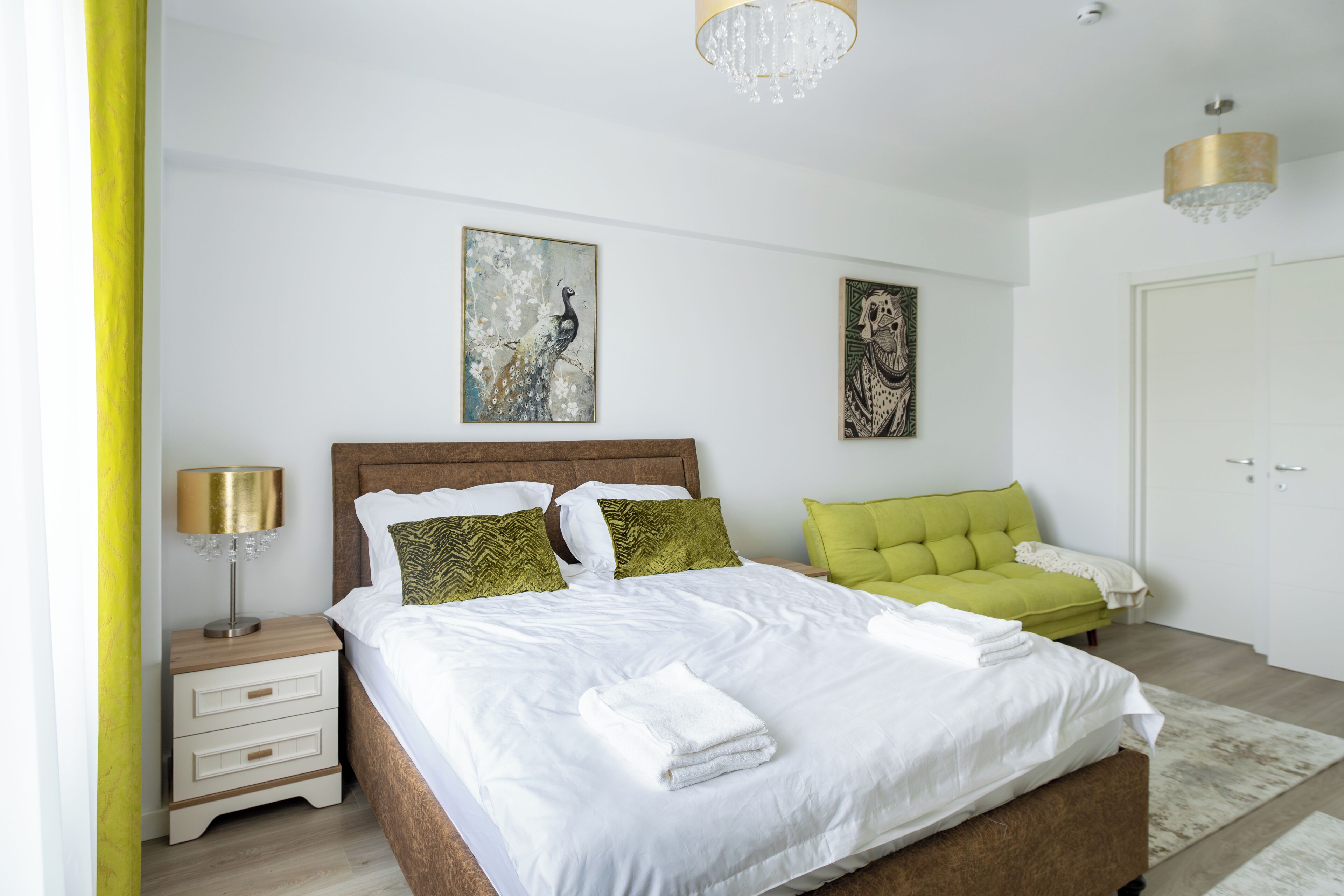 Een slaapkamer met een groot bed, een nachtkastje, een groene bank en kunstwerken aan de muur.