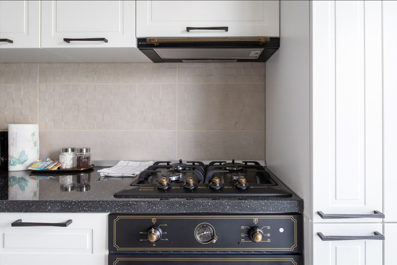 Cucina con piano cottura a gas, mobili bianchi e schienale piastrellato.