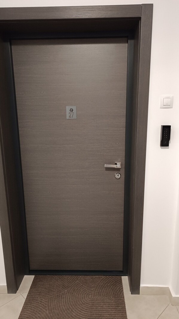A closed door with a numeric keypad lock, a doorbell, and a doormat.