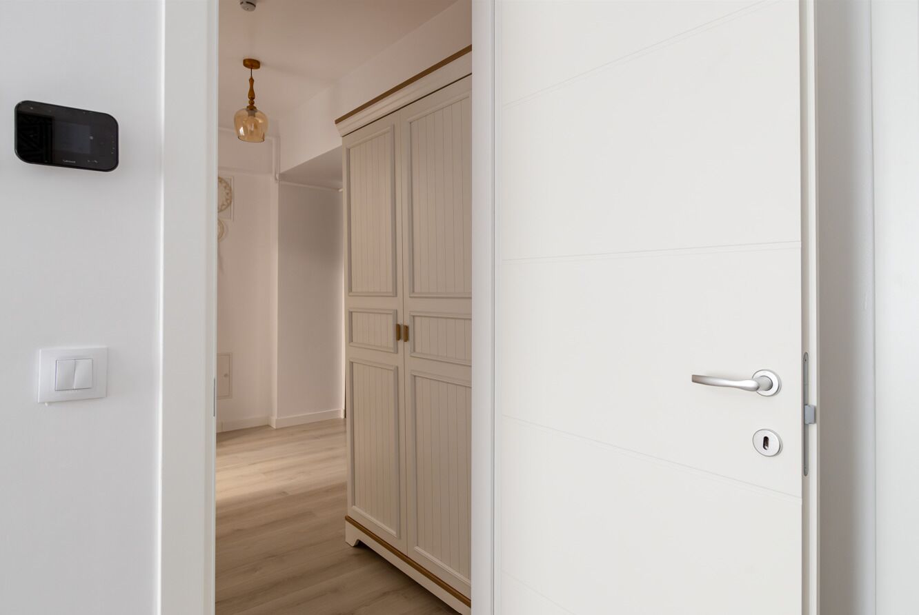 Ein Flur mit einer weißen Tür, einem Lichtschalter und einem Thermostat an der Wand.