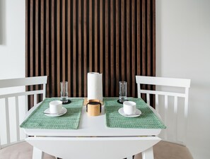 A dining table with two white chairs, a green placemat, a white napkin holder, and two glasses.