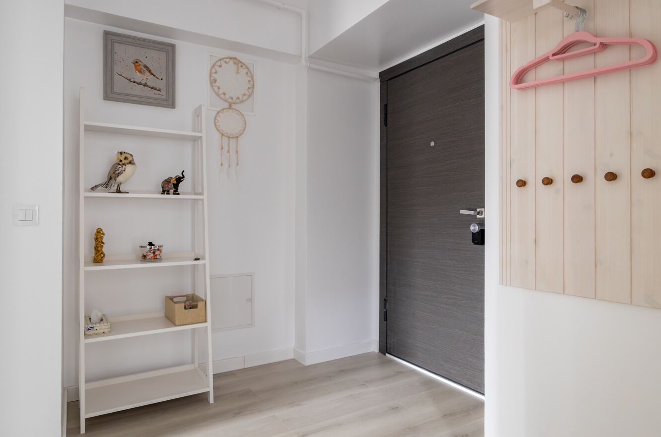 Un corridoio con un'unità di scaffalatura bianca, una porta in legno scuro e un appendino rosa al muro.