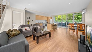A modern living room with a grey sofa, a coffee table, and a dining area with wooden chairs. - Spacious Apartment with Gym & Pool Access (City)