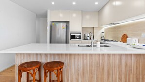 Una cocina moderna con una isla central, electrodomésticos de acero inoxidable y taburetes de bar de madera.