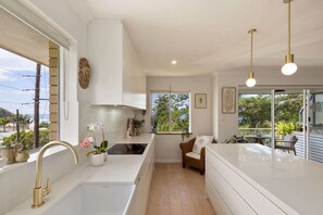 A modern kitchen with a large window, a built-in stove, and a white countertop. - Sunrise Cove 2-Bed Apartment at Newport Beach (Newport)