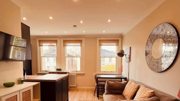 Una cucina moderna con isola centrale, zona pranzo con tavolo e sedie, divano in pelle marrone e un grande specchio decorativo a parete.