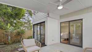 En moderne patio med fletmøbler, en ventilator i loftet og en skydedør til et indre rum.