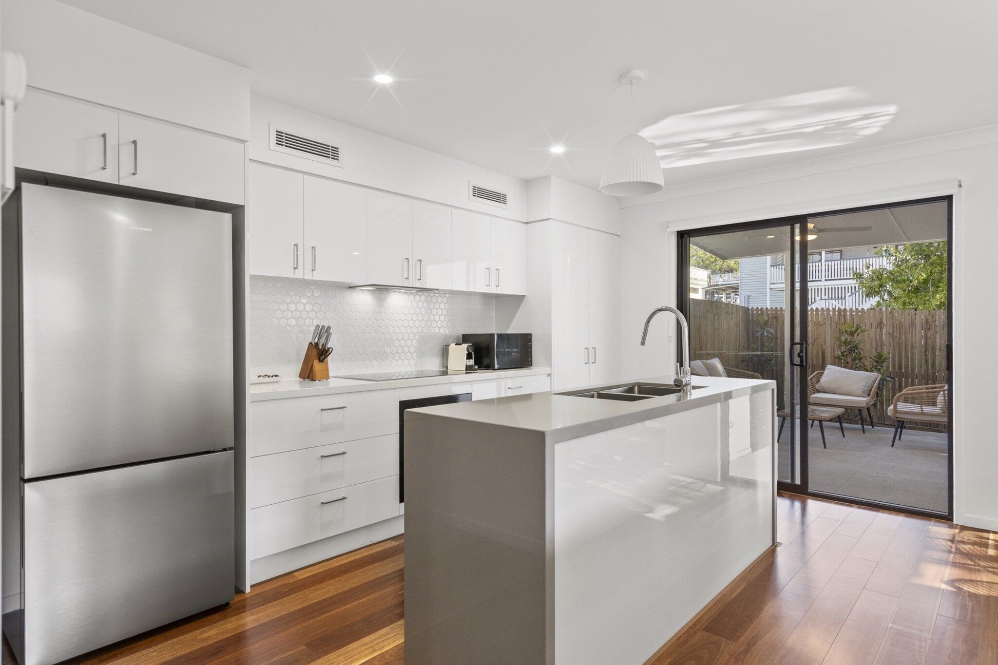 A modern kitchen with white cabinetry, a central island, and a sliding glass door leading to an outdoor patio area.