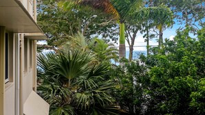 Un edificio con balcón que da a un exuberante jardín con diversas plantas y árboles tropicales.