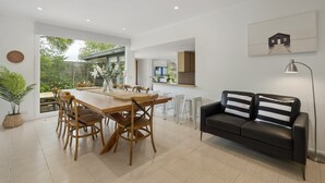 Un espace de repas moderne avec une table et des chaises en bois, un canapé en cuir noir et une grande fenêtre donnant sur un jardin.