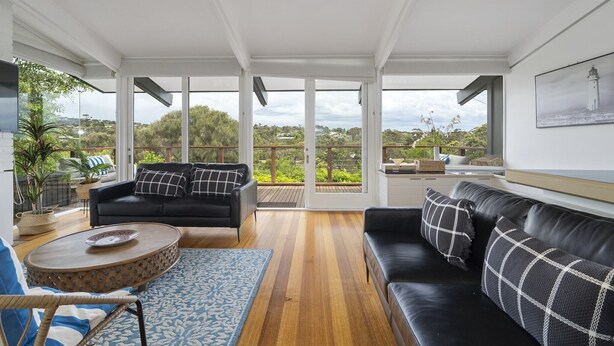 Un salon spacieux avec un canapé en cuir noir, une table basse ronde et une vue sur un jardin luxuriant, visible à travers de grandes portes vitrées.