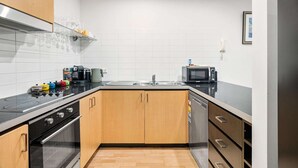 Una cocina moderna con encimera negra, electrodomésticos de acero inoxidable, armarios de madera y salpicadero de azulejos blancos.