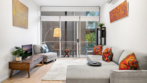 Una sala de estar moderna con un sofá gris, almohadas coloridas, una mesa de centro de madera, un televisor y una planta.
