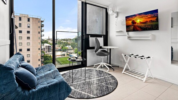 A modern living room with a large window, a sofa, a small table, a chair, a TV, and a drying rack. - South Melbourne Apartment with Gym Access (South Melbourne)
