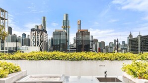 A city skyline with modern buildings, a concrete wall with greenery, and a metal structure in the foreground. - South Melbourne Apartment with Gym Access (South Melbourne)